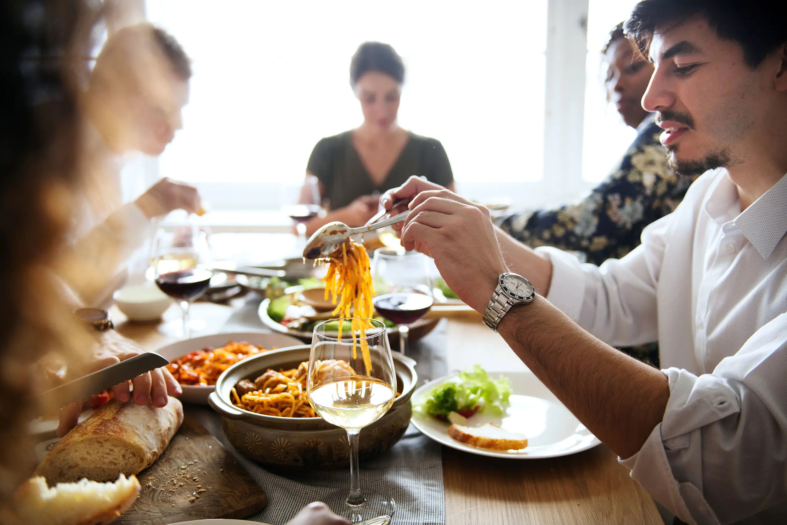 Group of people enjoying a meal together at a well-set dining table with various dishes and glasses of white wine.